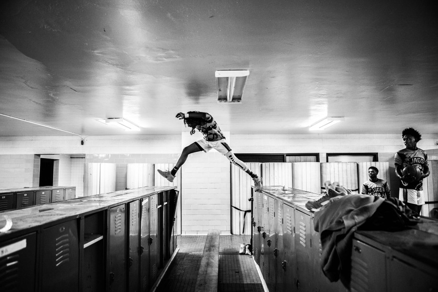 A young basketball player jumps from one set of lockers to another in a team locker room.