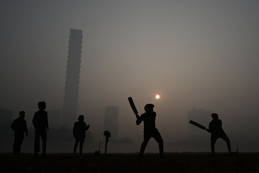 A small group of people play cricket in a park on a very foggy morning.