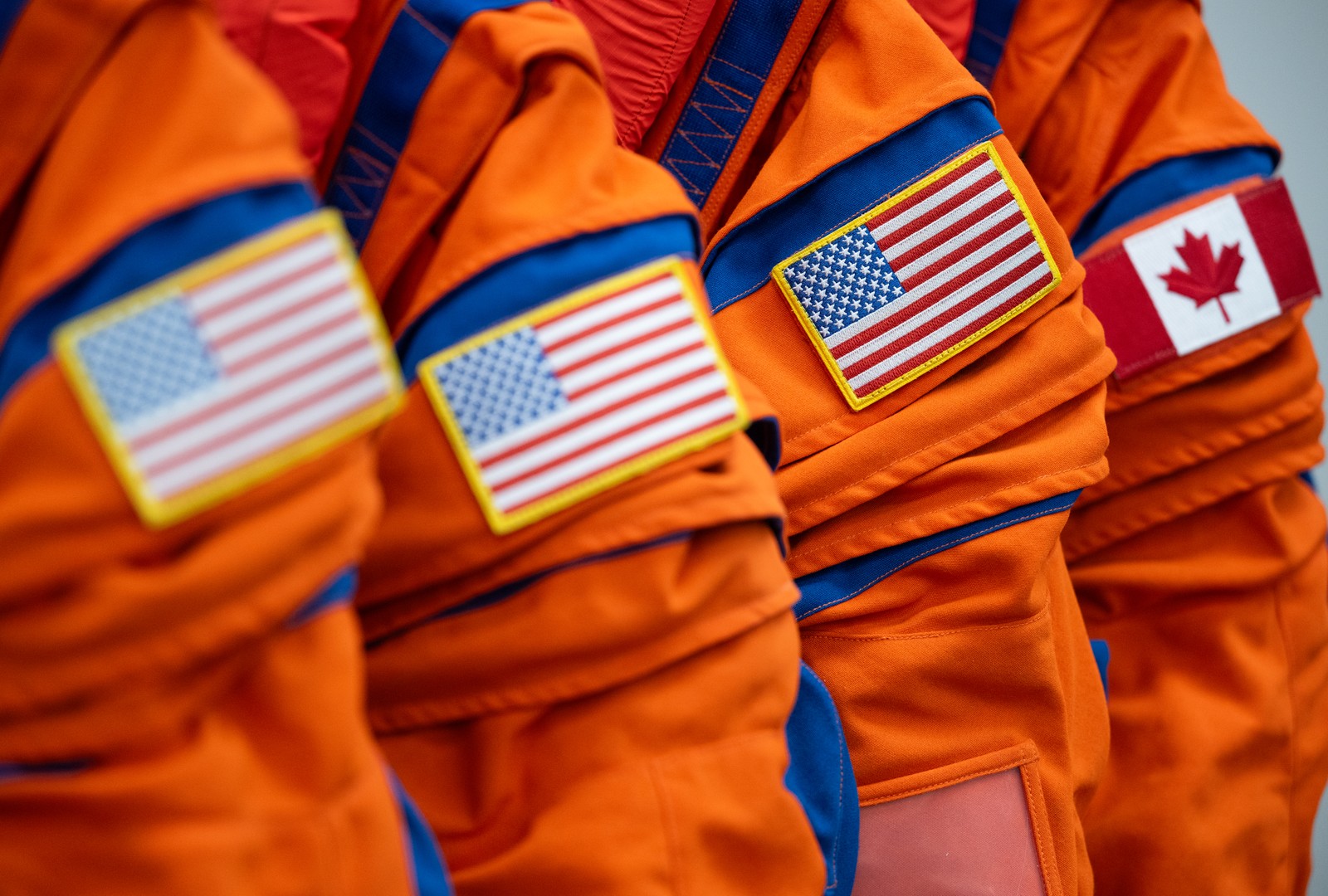 Three American flag arm patches and one Canadian flag arm patch are seen on the shoulders of four orange flight suits.