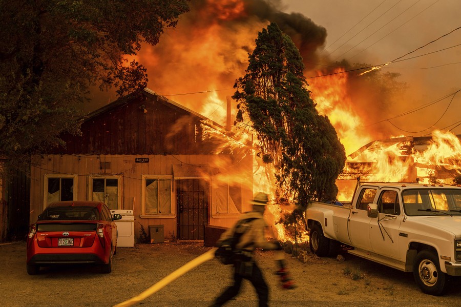 A firefighter moves in front of several burning structures.