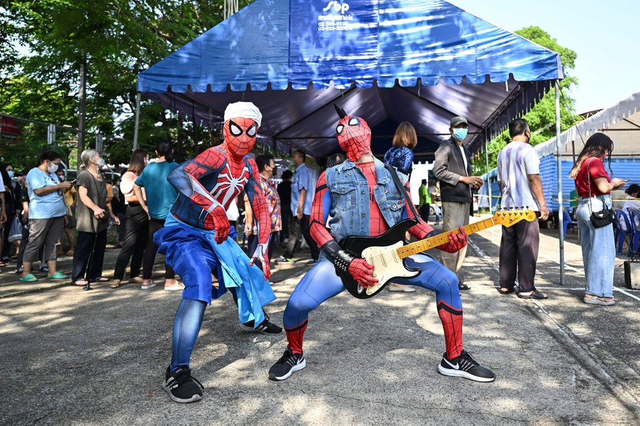 Two men dressed as Spiderman pose in front of a line of voters.