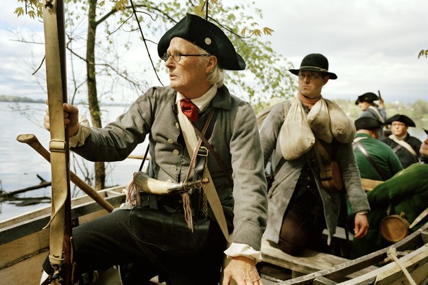 a group of reenactors posed in a wooden rowboat on a lake