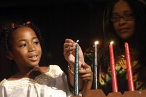 A child and adult lighting the Kwanzaa kinara