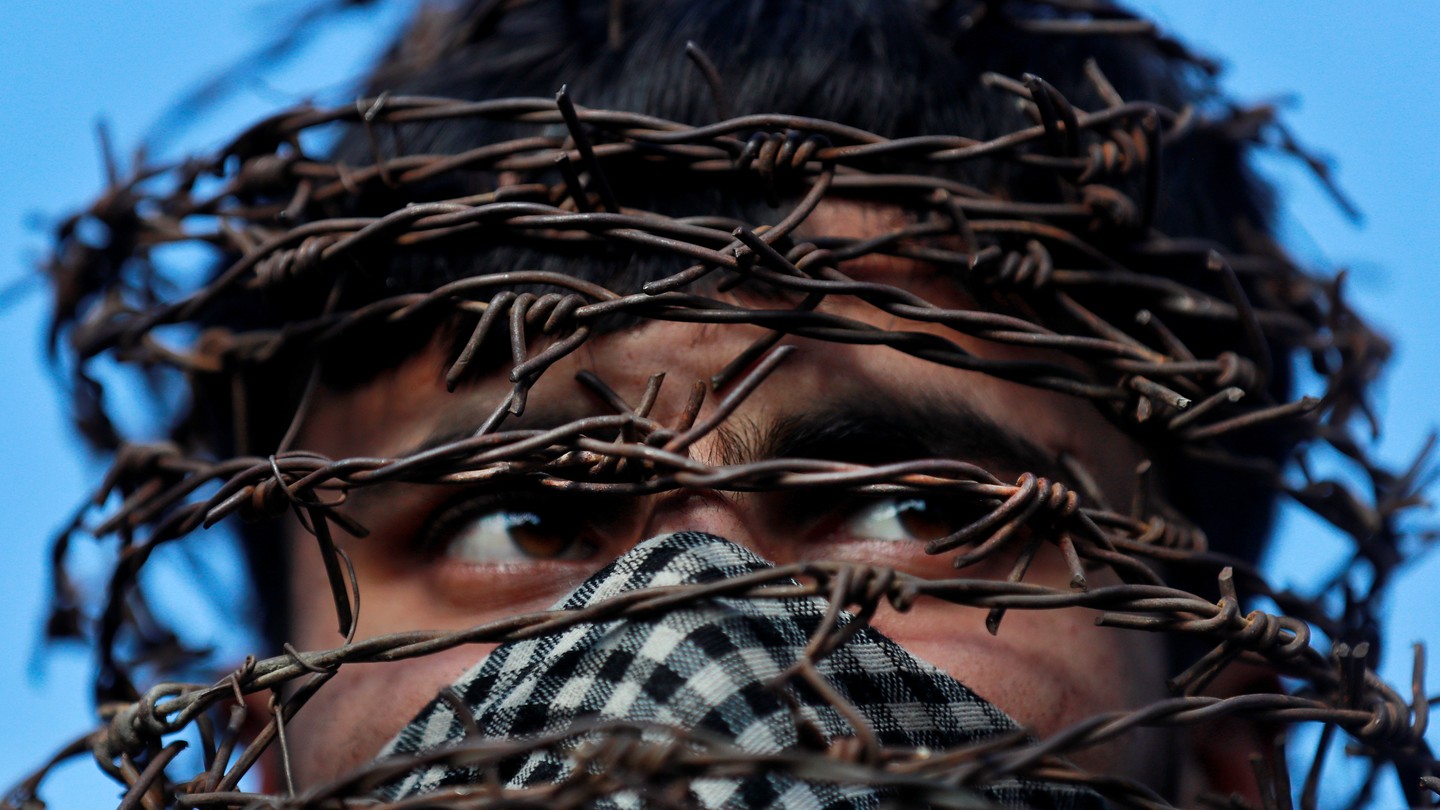 A masked Kashmiri man with his head covered with barbed wire attends a protest in Srinagar.