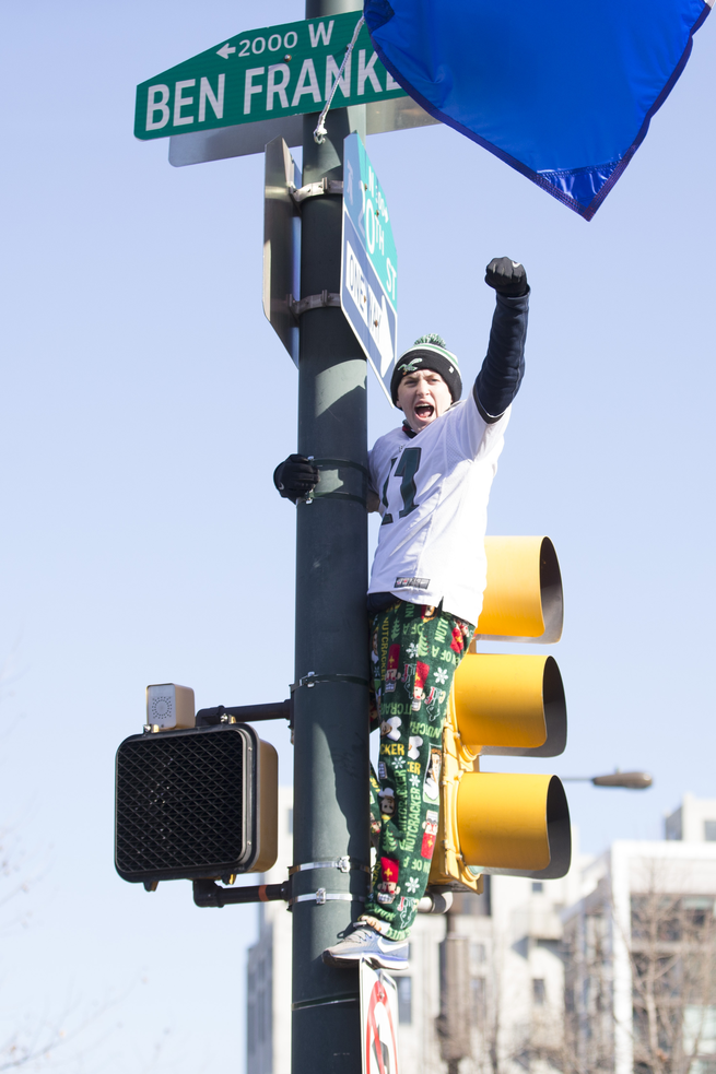photo of man in Eagles winter hat yelling with fist raised standing on top of a stoplight