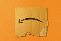 A torn piece of an Amazon box, the logo upside down, rests against an orange background.