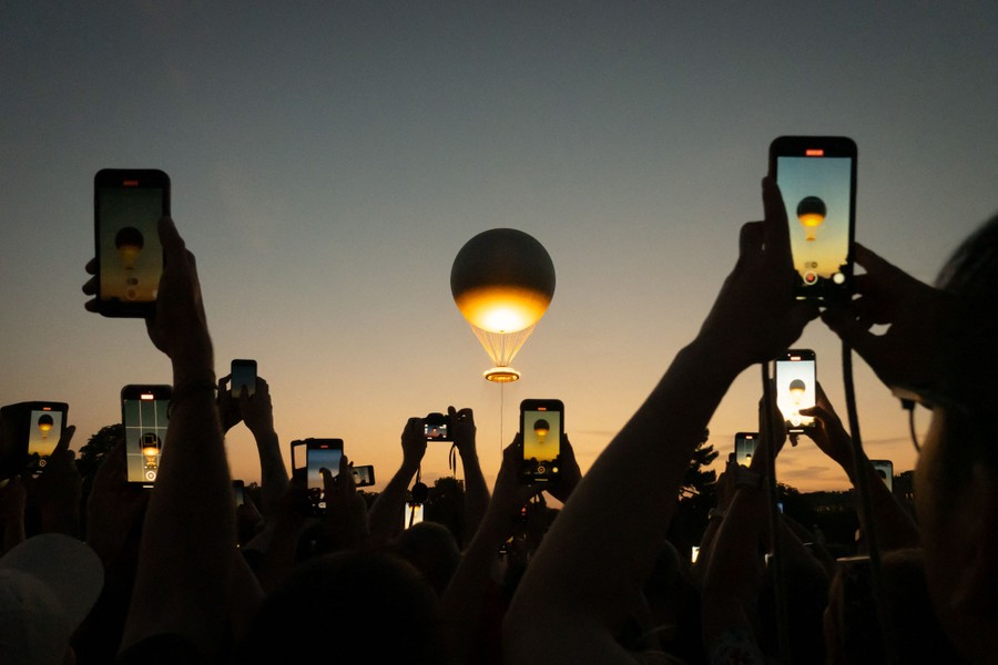 People take photos and video of a hot-air balloon carrying the Olympic cauldron.