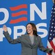Kamala Harris waving happily in front of a BIDEN HARRIS sign and an American flag