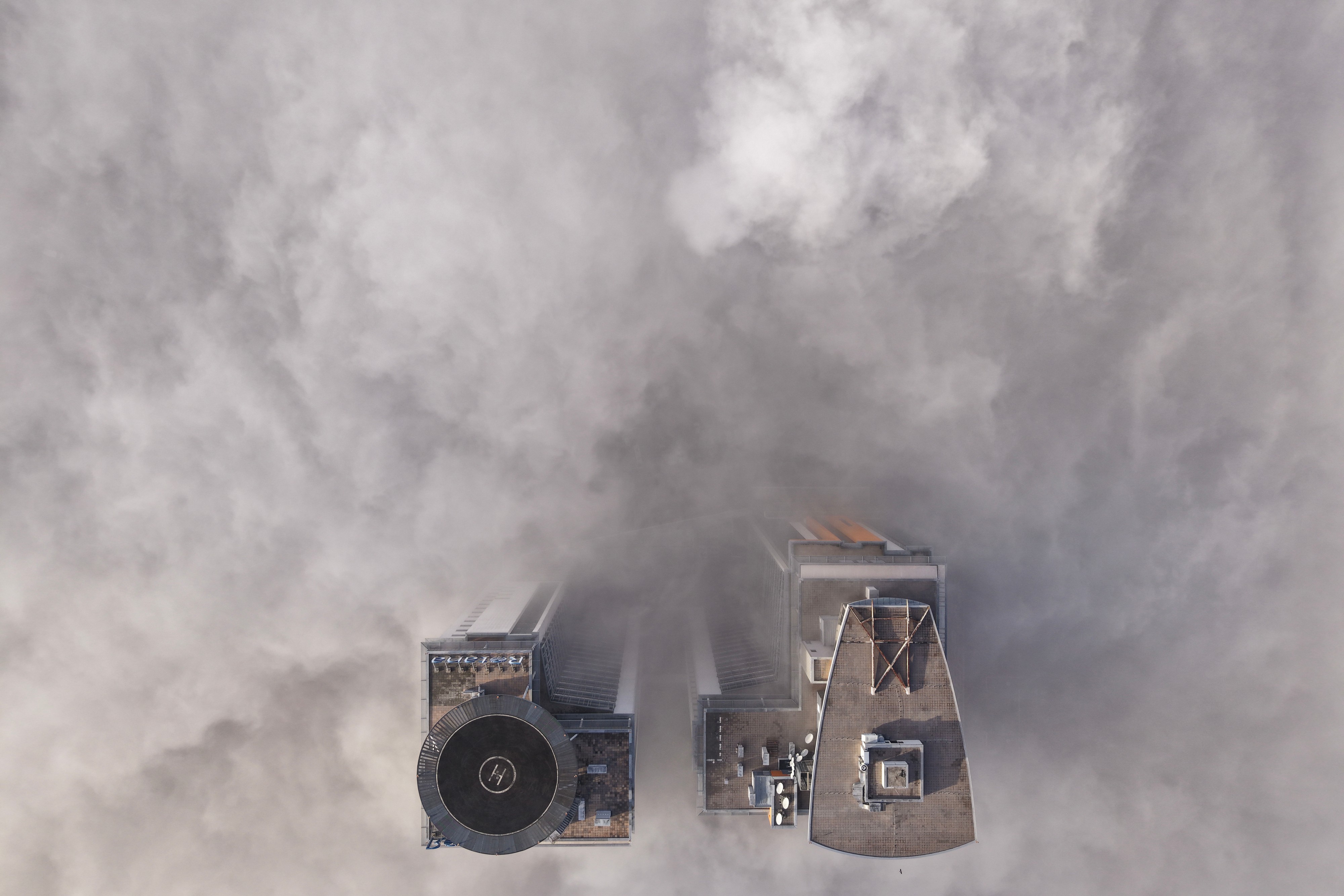 An aerial view of two tall buildings peeking through a dense layer of fog
