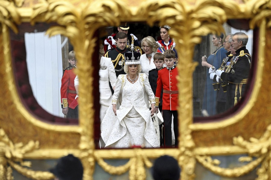 Queen Camilla walks down steps, seen through the windows of a waiting carriage.