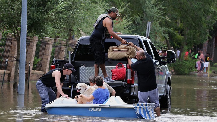 Five people load up duffel bags and a dog onto a truck bed in a flooded street.