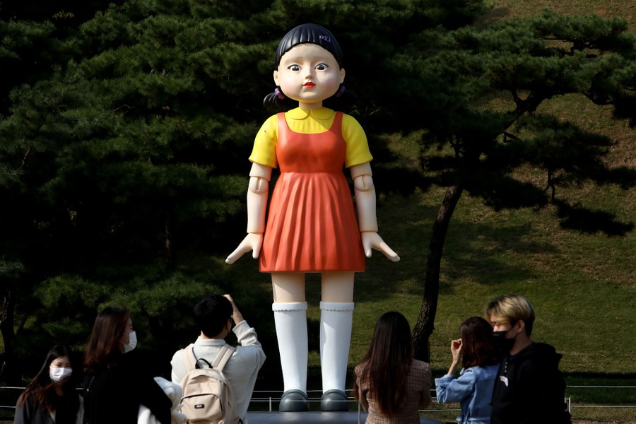 A large statue of a robot doll stands in a park.
