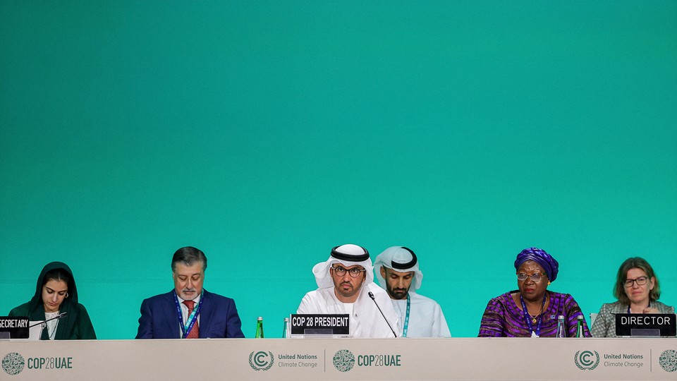 Sultan Al Jaber and other UN leaders sit at a table against a green background