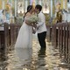 A newlywed couple kisses after a wedding ceremony inside a church that has been flooded, with about a foot of standing floodwater.