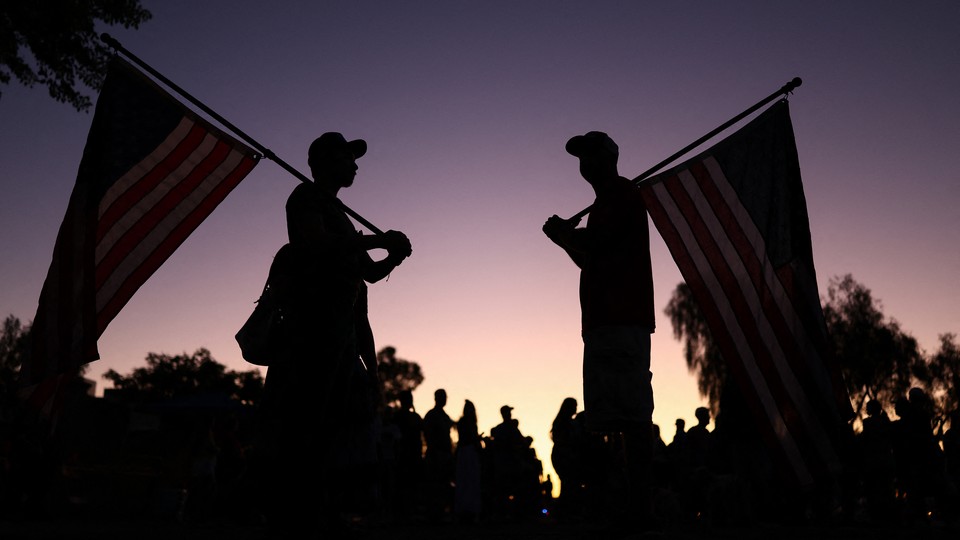 Photo of two men at sunset facing each other, holding American flags