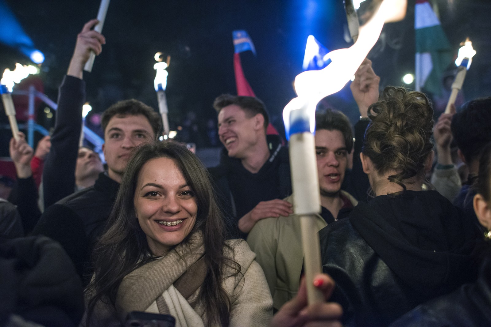 People celebrate, holding glowing torches and light tubes during a nighttime rally.