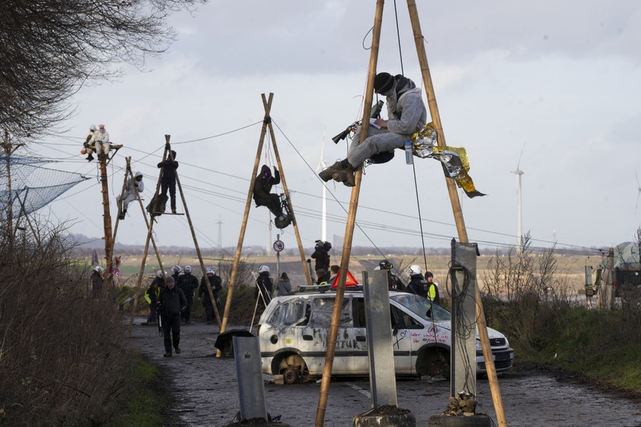 Protesters sit on ropes hanging from tall poles in a road.