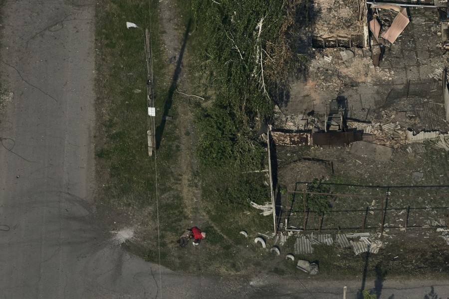 An aerial view of the bodies of two civilians lying beside a city street, near a small bomb crater