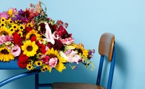 A profile view of a desk with flowers spilling off of it, against a blue background