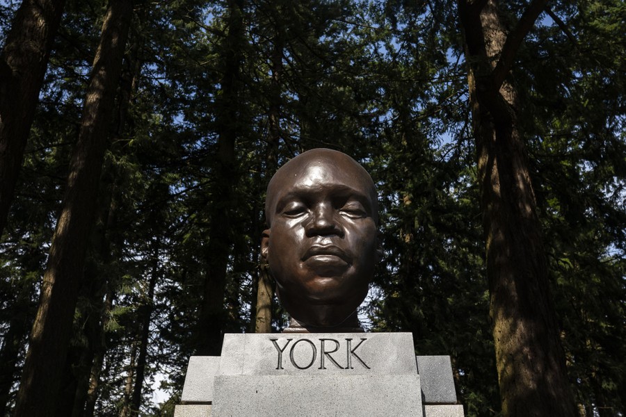 The bronze head of a person stands on a pedestal among trees.