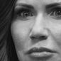 A close-up black-and-white photo of Kristi Noem's face