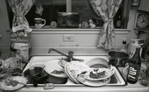 Black-and-white image of a sink overflowing with dirty dishes