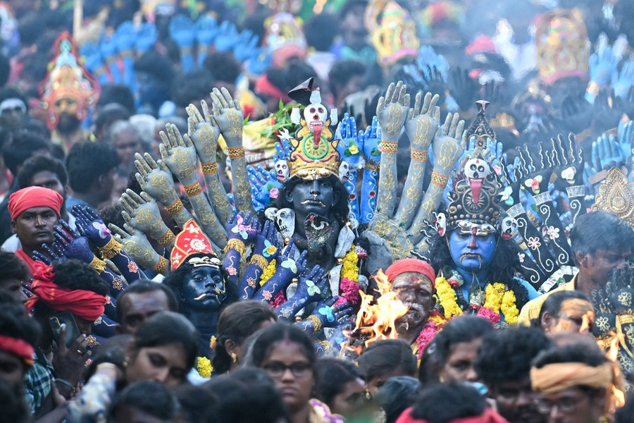 People parade through a crowd in costume, dressed as a many-armed Hindu goddess.