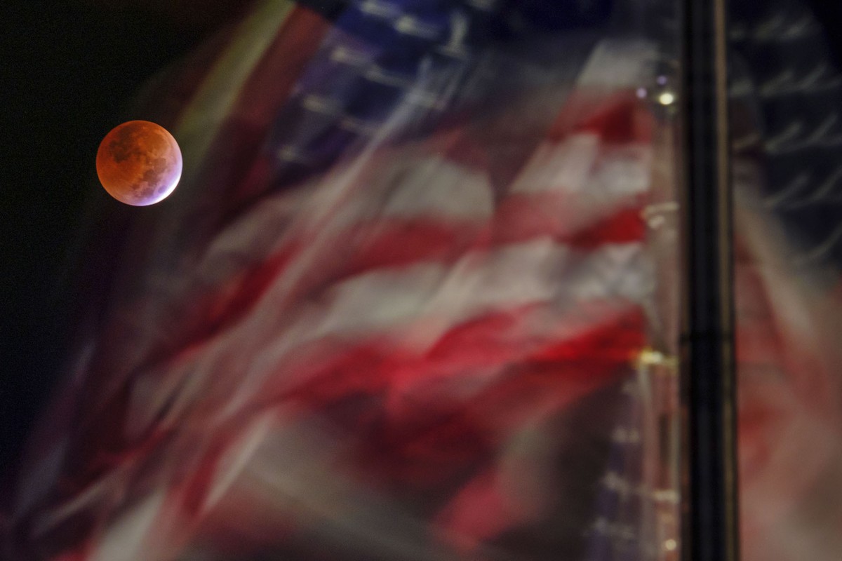 The reddish-colored full moon appears beyond flapping American flags.