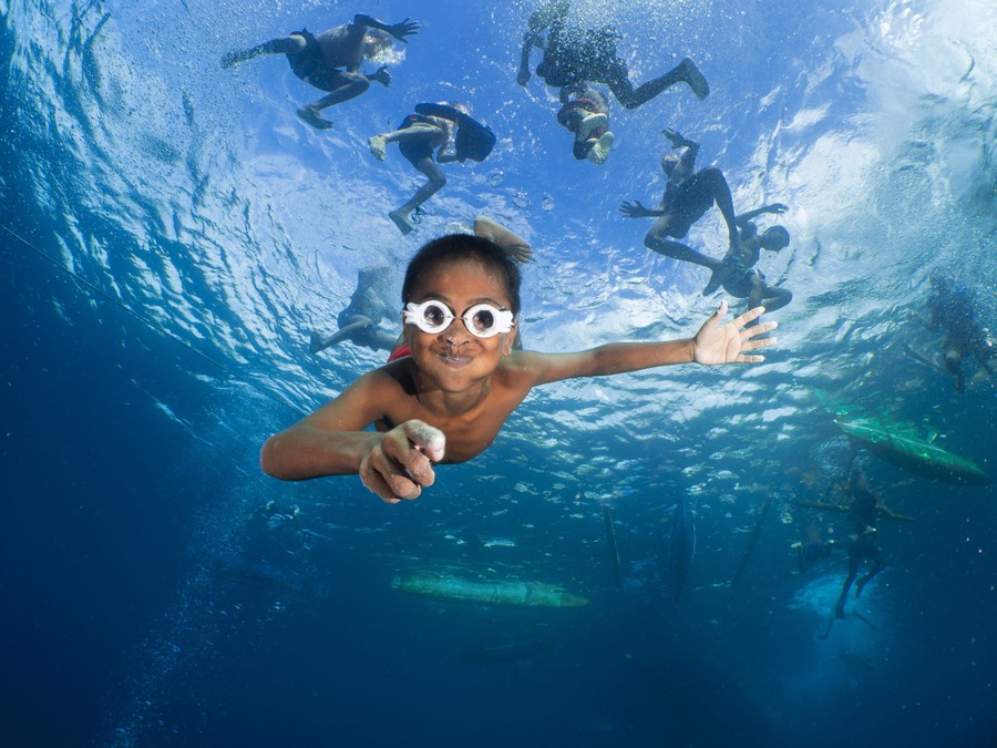 Un niño con gafas caseras se sumerge, visto bajo el agua.