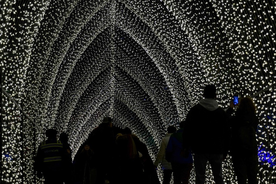 People walk beneath an arch made of strings of light.