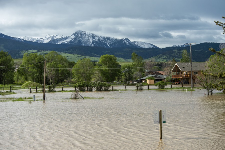 Standing floodwater surrounds trees and houses in a broad mountain valley.