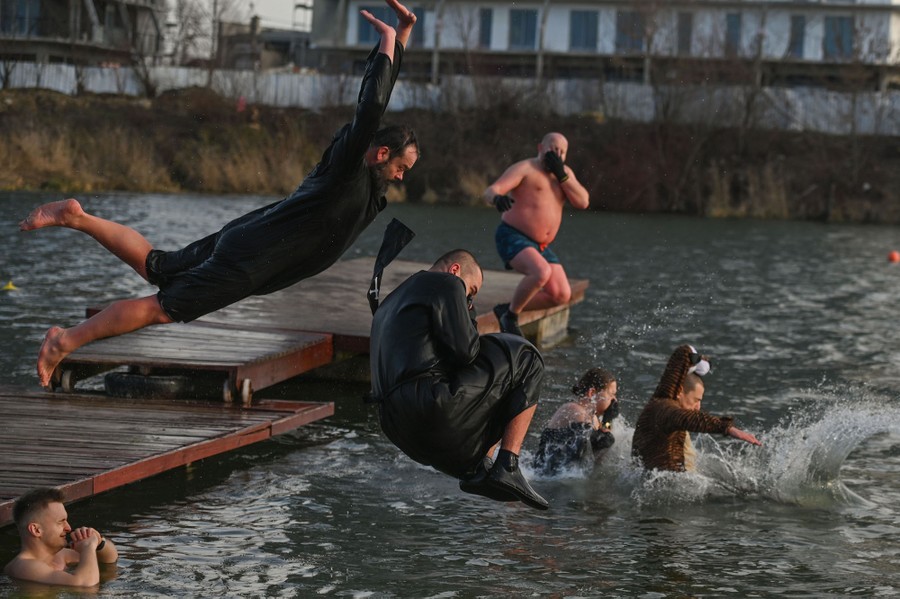 Several people leap playfully into a lake.