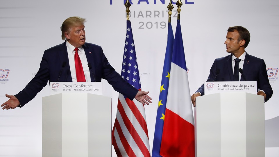 Donald Trump and Emmanuel Macron stand at lecterns as Trump delivers a speech.