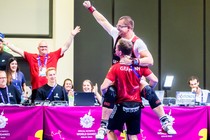 An athlete raises his arm in celebration while being lifted by a coach.
