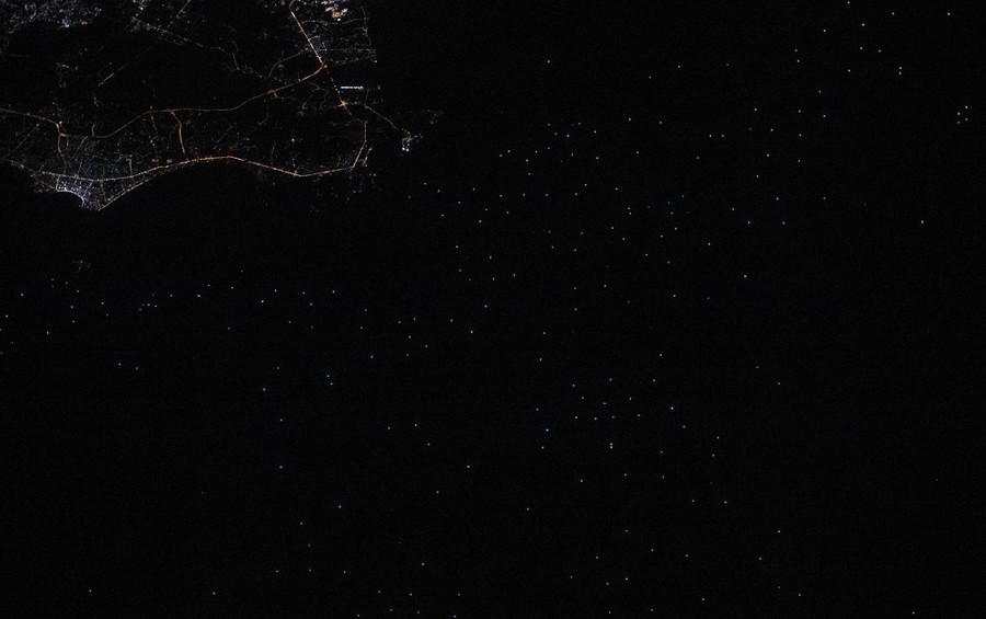 Many dots of light, visible near a coastline at night, seen from orbit.