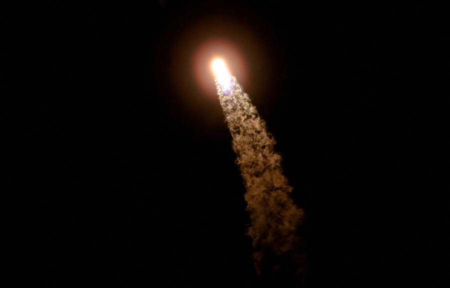 The bright plume of a rocket rises into a dark sky.