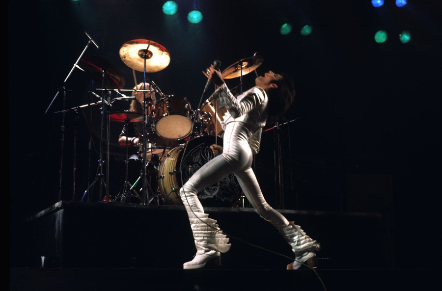 Freddie Mercury performs on stage in front of his drummer.