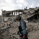An Afghan policeman walks past a ruined building and a pile of rubble.