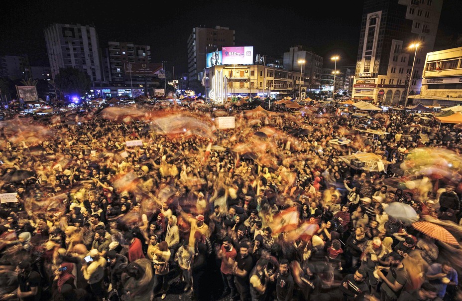A long-exposure photo taken on October 24, 2019, depicts Lebanese protesters waving national flags at Al-Nour Square, in Lebanon's northern city of Tripoli, on the eighth day of protests against tax increases and official corruption.
