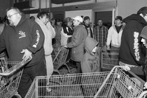 Customers push shopping carts while crowded in a small room.