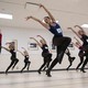 About a dozen dancers perform together in a studio during an audition.