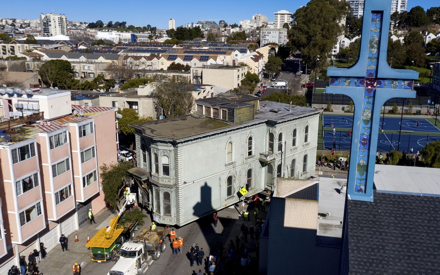 An old two-story house is towed through a city street.