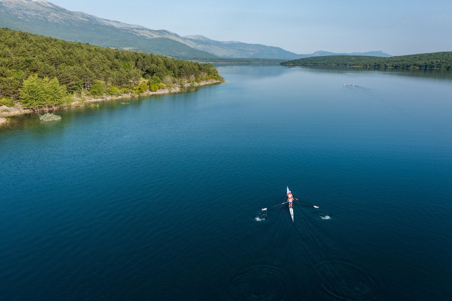 Rowers navigate across a large, quiet lake.