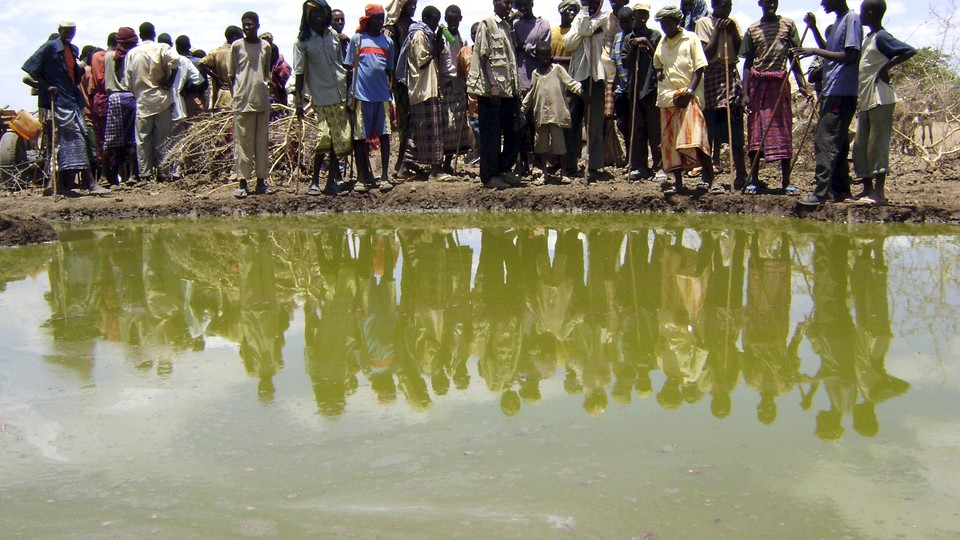 A group of people gather around a small, cloudy body of water.