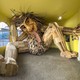 A large wooden troll sculpture sits inside a room, looking cramped, its head against the ceiling.