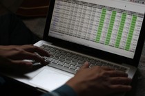 Someone's hands rest on a laptop displaying a large spreadsheet.