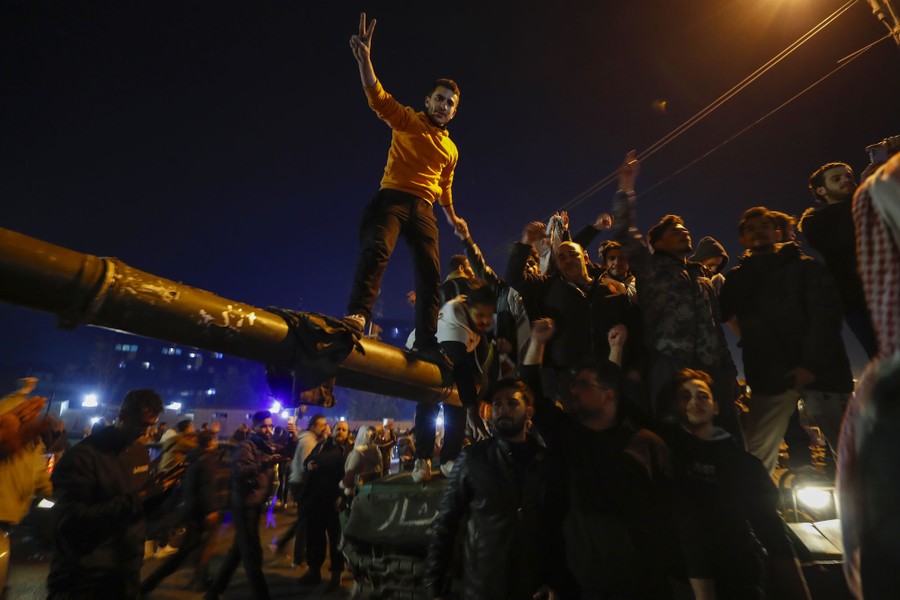 A crowd of civilians gathers around and on top of a tank in a street.