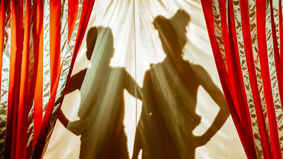 The silhouettes of a woman and a child behind red-and-gold-striped curtains