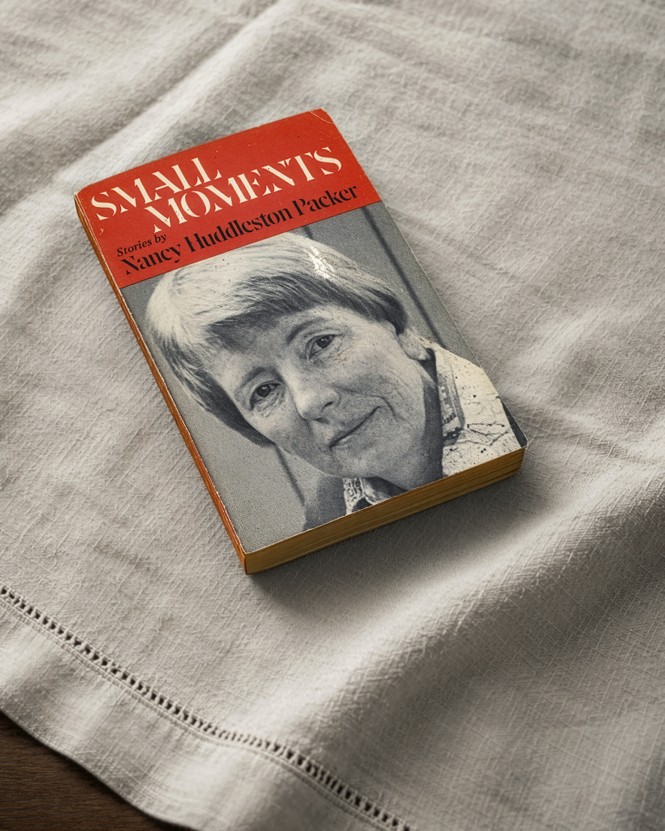 photo of paperback book 'Small Moments' by Nancy Huddleston Packer with the author's portrait on the cover, laid on white linen tablecloth