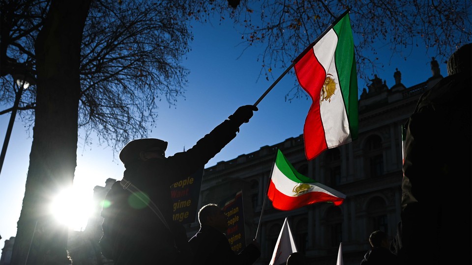 People in shadow hold up three-colored flags in front of a stately building.